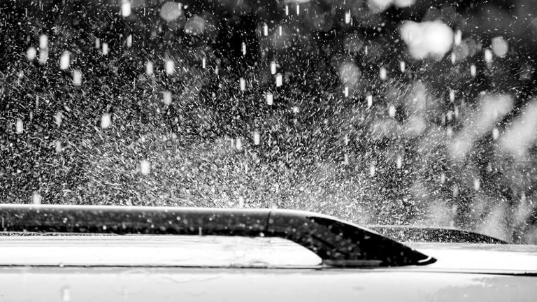 Black and white photo of hail stones falling on roof of car.