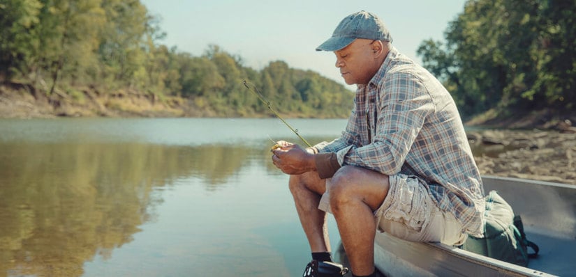 Man sitting on edge of tinny setting lure before fishing