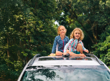 Kids sitting and laughing on the roof of a car in front of tree
