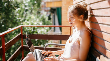 A woman sitting on her laptop in the sun, researching whether she needs home insurance if she already has body corporate insurance