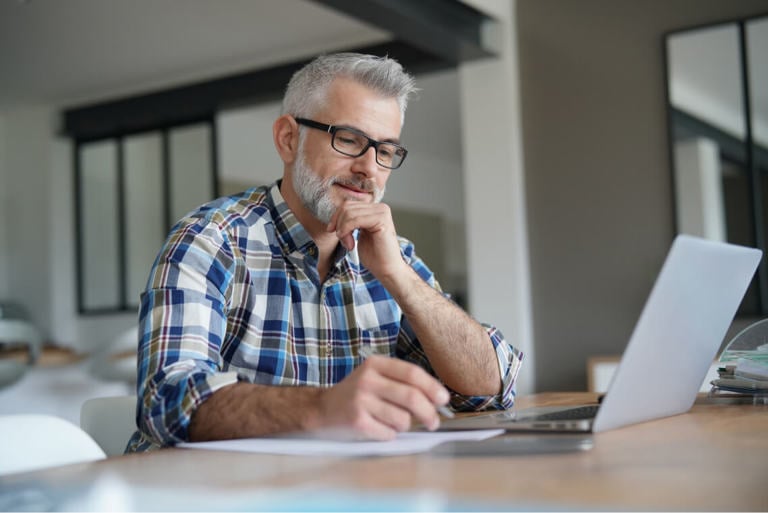 A grey haired man researching on a laptop.