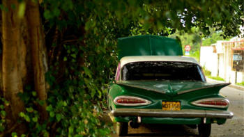 An old green coloured hotrod car parked in the street.  