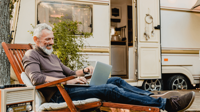Man sitting  with his laptop on a wooden lounger just outside of his caravan