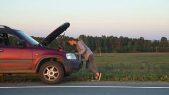 A woman looking under a car bonnet. 